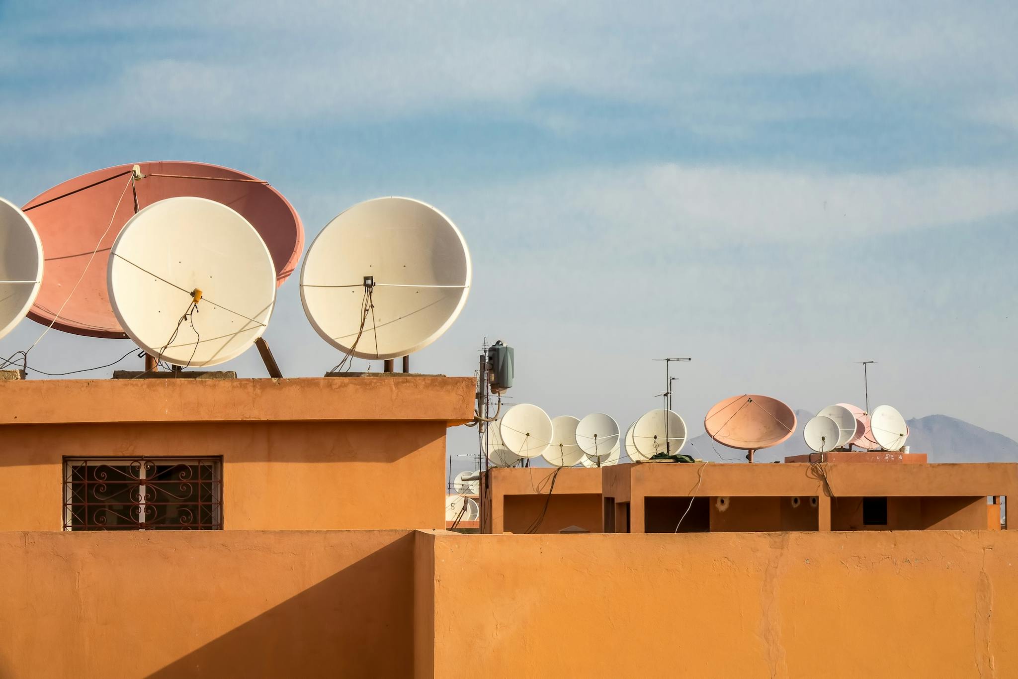 Multiple satellite dishes on orange rooftops under a clear blue sky, capturing urban connectivity.