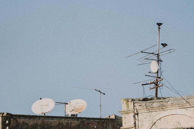 Old rooftop with satellite dishes and antennas under a clear blue sky.