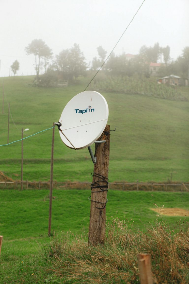 Satellite dish on a wooden pole in a rustic, fog-covered countryside setting.