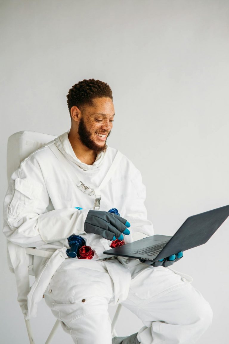 Smiling man in a space suit using a laptop, indoors setting.